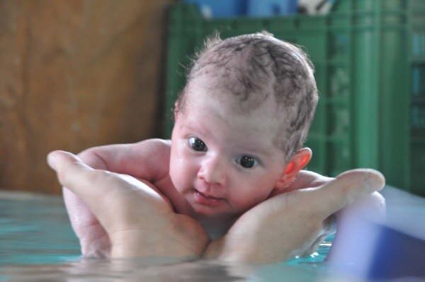 Bimbo in acqua sorretto dalle mani di un adulto